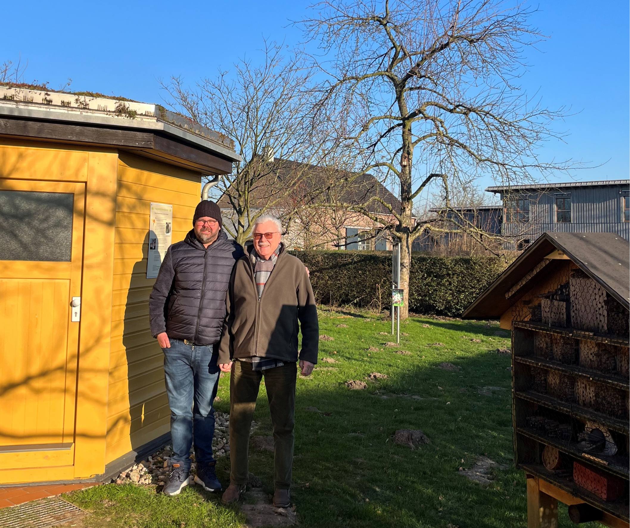 Zwei Männer stehen vor einem gelben Haus, einem Bienenhaus.